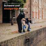 Zwei Magnetfischer ziehen eine schwere antike Nähmaschine mit einem Magnetar Bergemagneten und orangefarbenem Seil aus der Gracht.